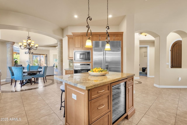 kitchen with pendant lighting, decorative columns, a center island, built in appliances, and wine cooler