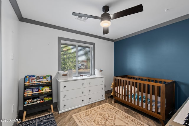 bedroom featuring wood finished floors, a nursery area, ceiling fan, baseboards, and visible vents