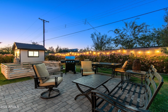 patio terrace at dusk with a grill, outdoor dining area, and an outdoor structure
