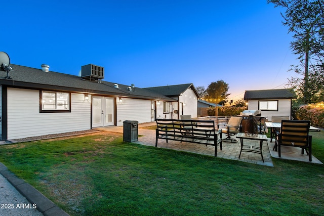 back of property at dusk with a patio, outdoor lounge area, central AC, and a lawn