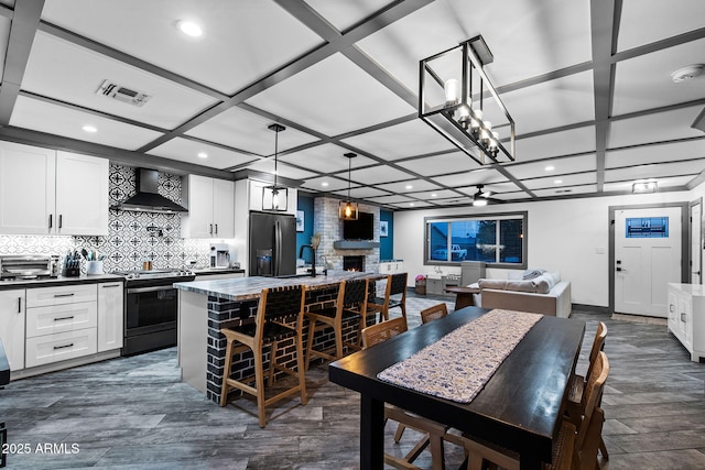 kitchen with wall chimney range hood, visible vents, electric range oven, a fireplace, and black fridge