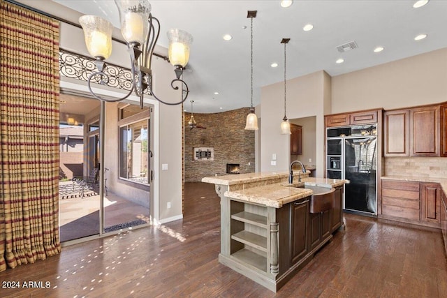 kitchen with hanging light fixtures, a center island with sink, black fridge, dark hardwood / wood-style floors, and sink