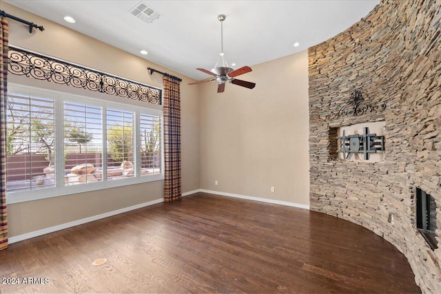 unfurnished living room featuring a stone fireplace, ceiling fan, and dark hardwood / wood-style flooring