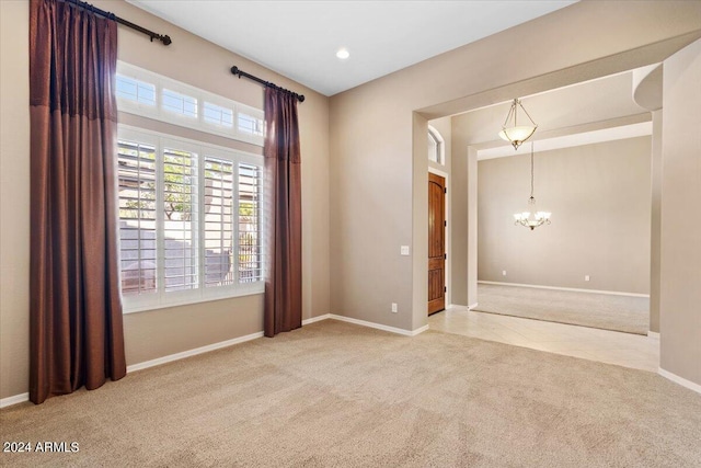 spare room featuring a notable chandelier and light colored carpet