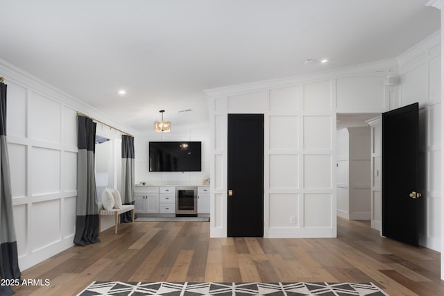 unfurnished living room with wine cooler, ornamental molding, vaulted ceiling, and light hardwood / wood-style floors