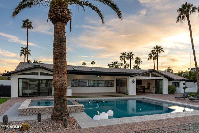 pool at dusk featuring a patio and an in ground hot tub