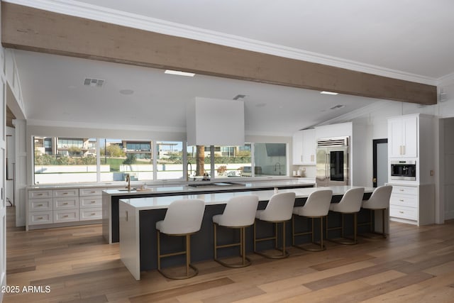 kitchen with lofted ceiling, white cabinetry, crown molding, light wood-type flooring, and stainless steel appliances