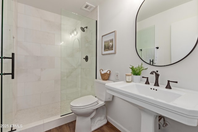 bathroom featuring wood-type flooring, tiled shower, and toilet