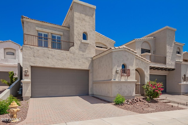 view of front of house with stucco siding, decorative driveway, a balcony, and an attached garage