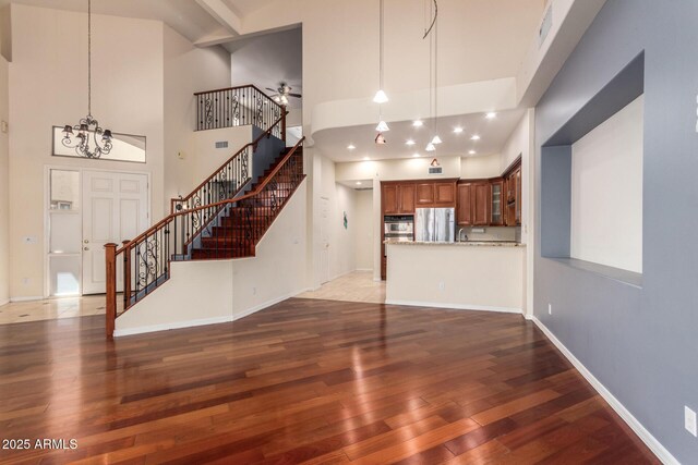 unfurnished living room with a towering ceiling, wood finished floors, stairway, and ceiling fan with notable chandelier
