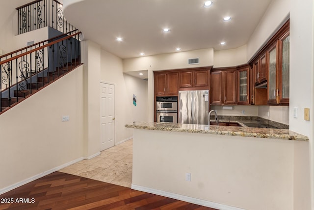 kitchen featuring glass insert cabinets, light stone countertops, stainless steel appliances, and light wood-style floors