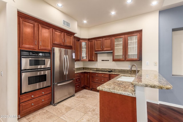 kitchen with light stone counters, a sink, appliances with stainless steel finishes, visible vents, and a peninsula