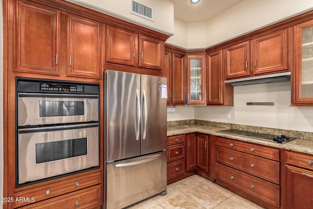 kitchen featuring light stone counters, glass insert cabinets, appliances with stainless steel finishes, visible vents, and under cabinet range hood