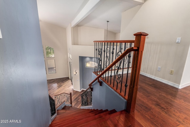 stairway featuring baseboards, wood finished floors, and a high ceiling