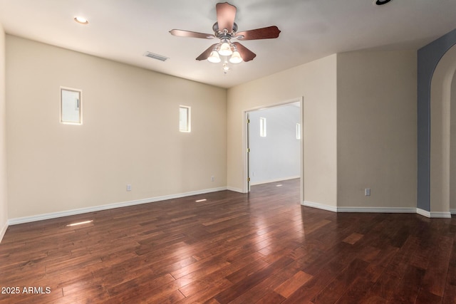 unfurnished room with arched walkways, baseboards, visible vents, a ceiling fan, and dark wood-type flooring