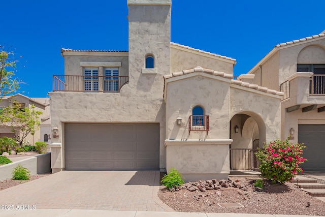 view of front of property featuring decorative driveway, a garage, stucco siding, and a balcony
