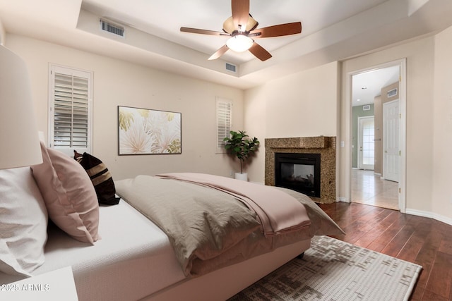 bedroom with baseboards, visible vents, wood-type flooring, and a tray ceiling