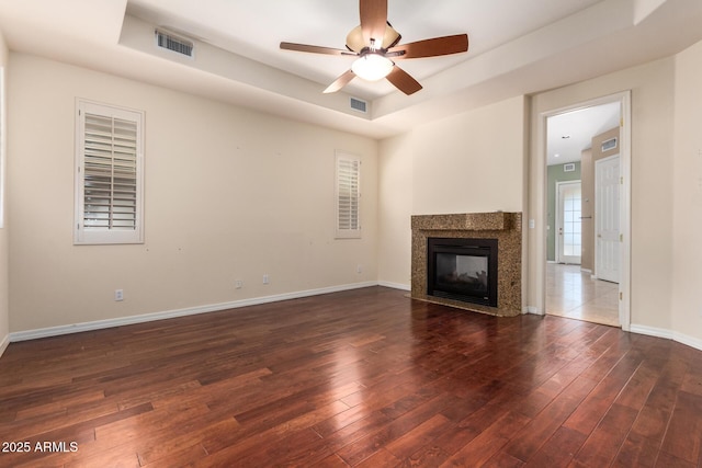 unfurnished living room with visible vents, a premium fireplace, wood-type flooring, and a tray ceiling