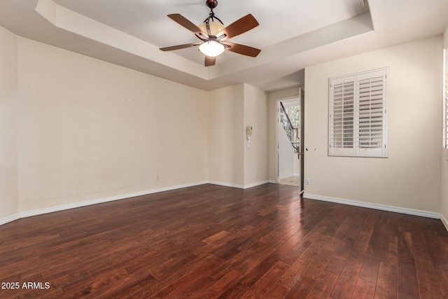 unfurnished room with a raised ceiling, ceiling fan, dark wood-style floors, and baseboards