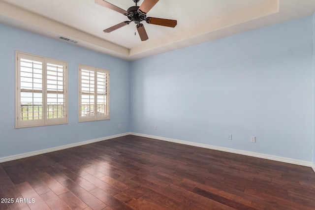 unfurnished room with dark wood-style floors, visible vents, a healthy amount of sunlight, and a tray ceiling