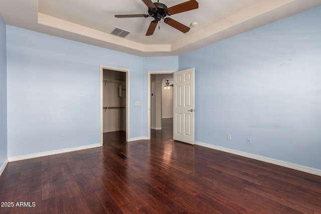 unfurnished bedroom with baseboards, visible vents, wood-type flooring, and a tray ceiling
