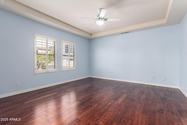 spare room with visible vents, ceiling fan, dark wood-style flooring, and a tray ceiling
