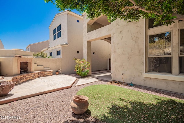 back of house featuring stucco siding, a patio area, and exterior fireplace