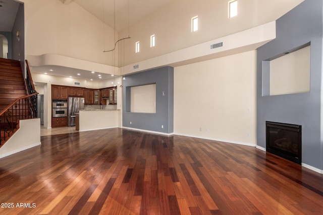 unfurnished living room featuring a glass covered fireplace, stairs, high vaulted ceiling, and dark wood finished floors