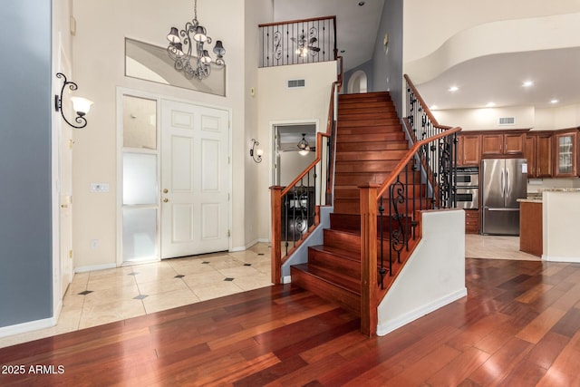 foyer entrance with baseboards, visible vents, stairway, and a towering ceiling