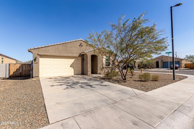 view of front facade with stucco siding, fence, a garage, driveway, and a tiled roof