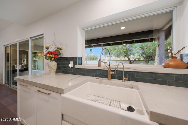 kitchen with a healthy amount of sunlight, white cabinetry, a sink, and light stone countertops