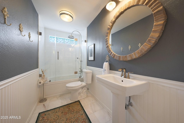 full bath with toilet, shower / bath combination with glass door, a sink, and wainscoting