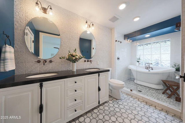 full bathroom with double vanity, recessed lighting, visible vents, a freestanding bath, and a sink