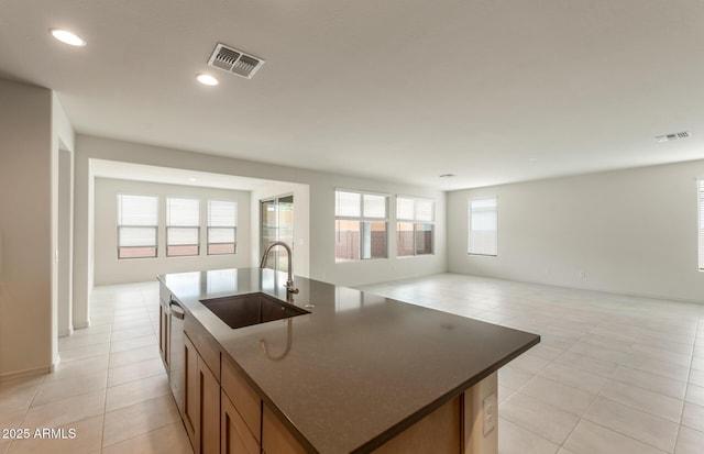 kitchen with sink, light tile patterned floors, a healthy amount of sunlight, and a center island with sink