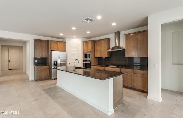 kitchen featuring appliances with stainless steel finishes, sink, decorative backsplash, a kitchen island with sink, and wall chimney range hood