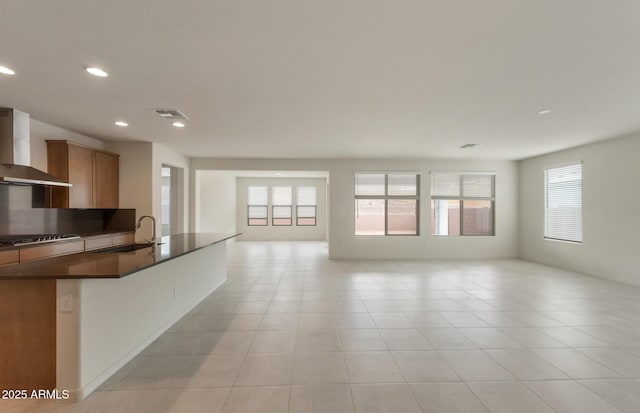 kitchen featuring light tile patterned floors, stainless steel gas stovetop, sink, and wall chimney range hood