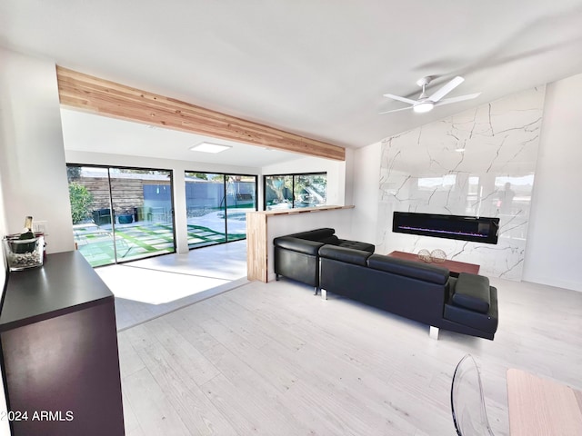 living room featuring lofted ceiling with beams, ceiling fan, light wood-type flooring, and a premium fireplace