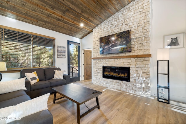 living area with wood ceiling, high vaulted ceiling, wood finished floors, and a stone fireplace