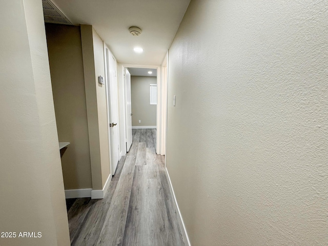 hallway with visible vents, baseboards, dark wood-style flooring, and a textured wall