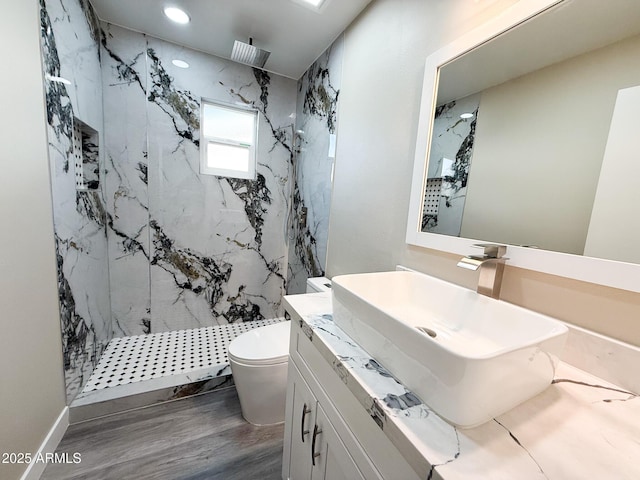 bathroom featuring vanity, wood finished floors, a marble finish shower, recessed lighting, and toilet