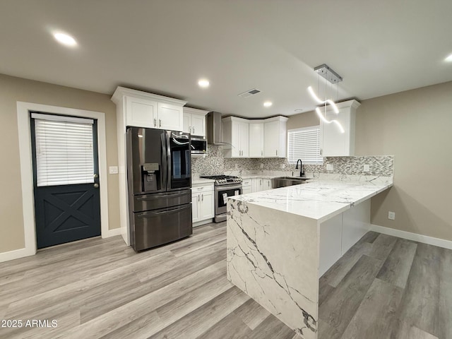 kitchen with a sink, backsplash, appliances with stainless steel finishes, a peninsula, and wall chimney range hood