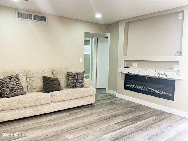 living room featuring a glass covered fireplace, wood finished floors, visible vents, and baseboards