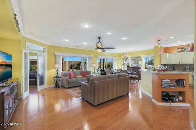 living room featuring ceiling fan with notable chandelier, light hardwood / wood-style flooring, and ornamental molding