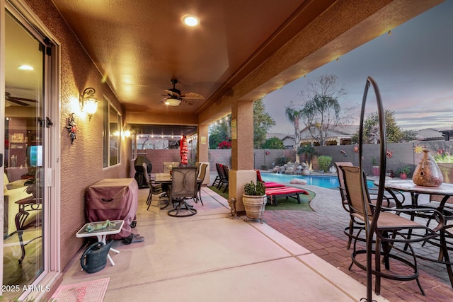 patio terrace at dusk with a fenced in pool, a fenced backyard, and a ceiling fan