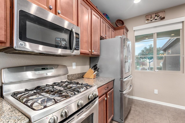 kitchen featuring brown cabinets, baseboards, stainless steel appliances, and light stone counters