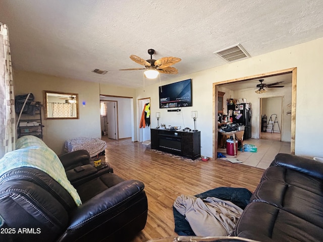 living room featuring ceiling fan, a textured ceiling, and light wood-type flooring