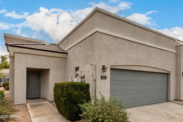 view of front of property with stucco siding, driveway, a tile roof, and a garage