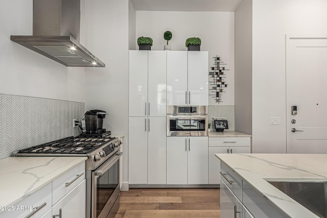 3131 N Central Ave Unit 7004, Phoenix, AZ 85012 - kitchen with gas range, wall chimney range hood, tasteful backsplash, light wood-style flooring, and white cabinetry