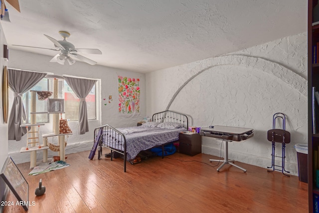 bedroom with a textured ceiling, wood-type flooring, and ceiling fan