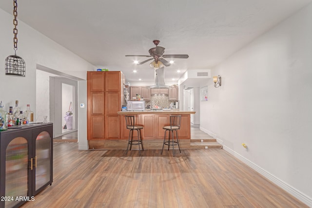 kitchen featuring hardwood / wood-style flooring, ceiling fan, a kitchen bar, and backsplash